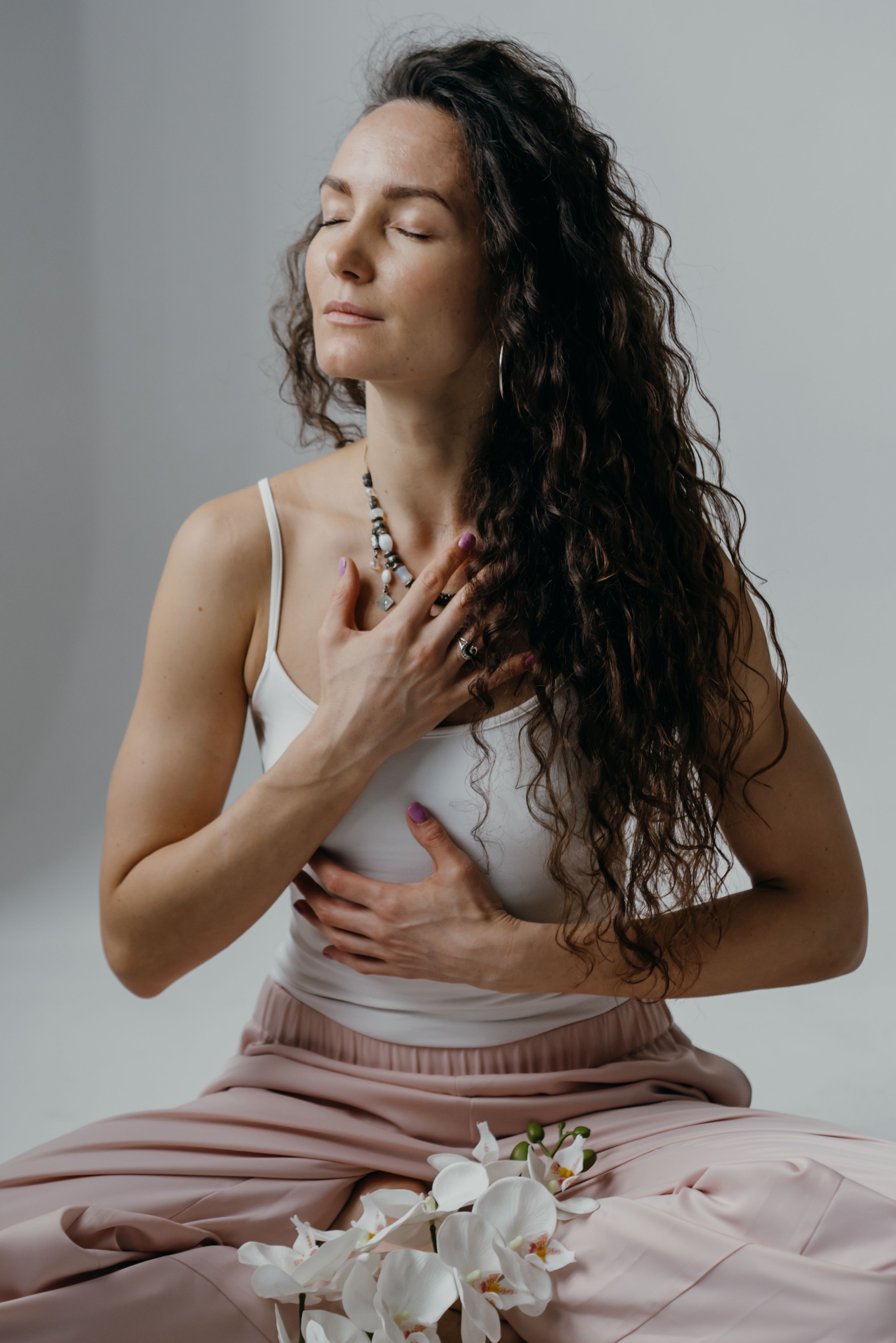 A woman seated with one hand on her heart and one on her belly